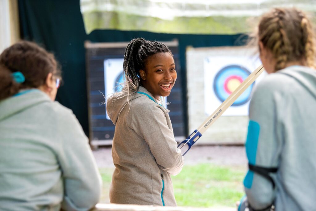 3 Rangers on an archery range - two have their backs to the camera and one has turned around to talk to her friends.