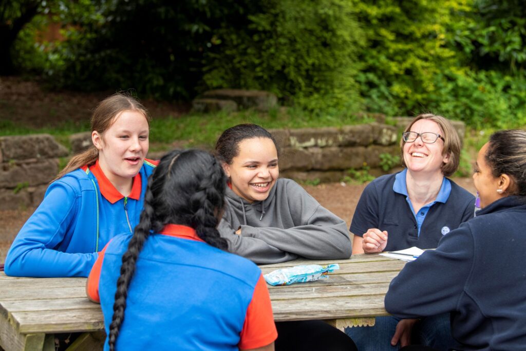 3 Guides sitting outside at a picnic bench, laughing with two of their leaders.